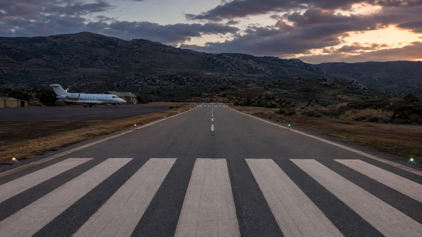 Short regional runway at dusk with terrain rising beyond the far threshold